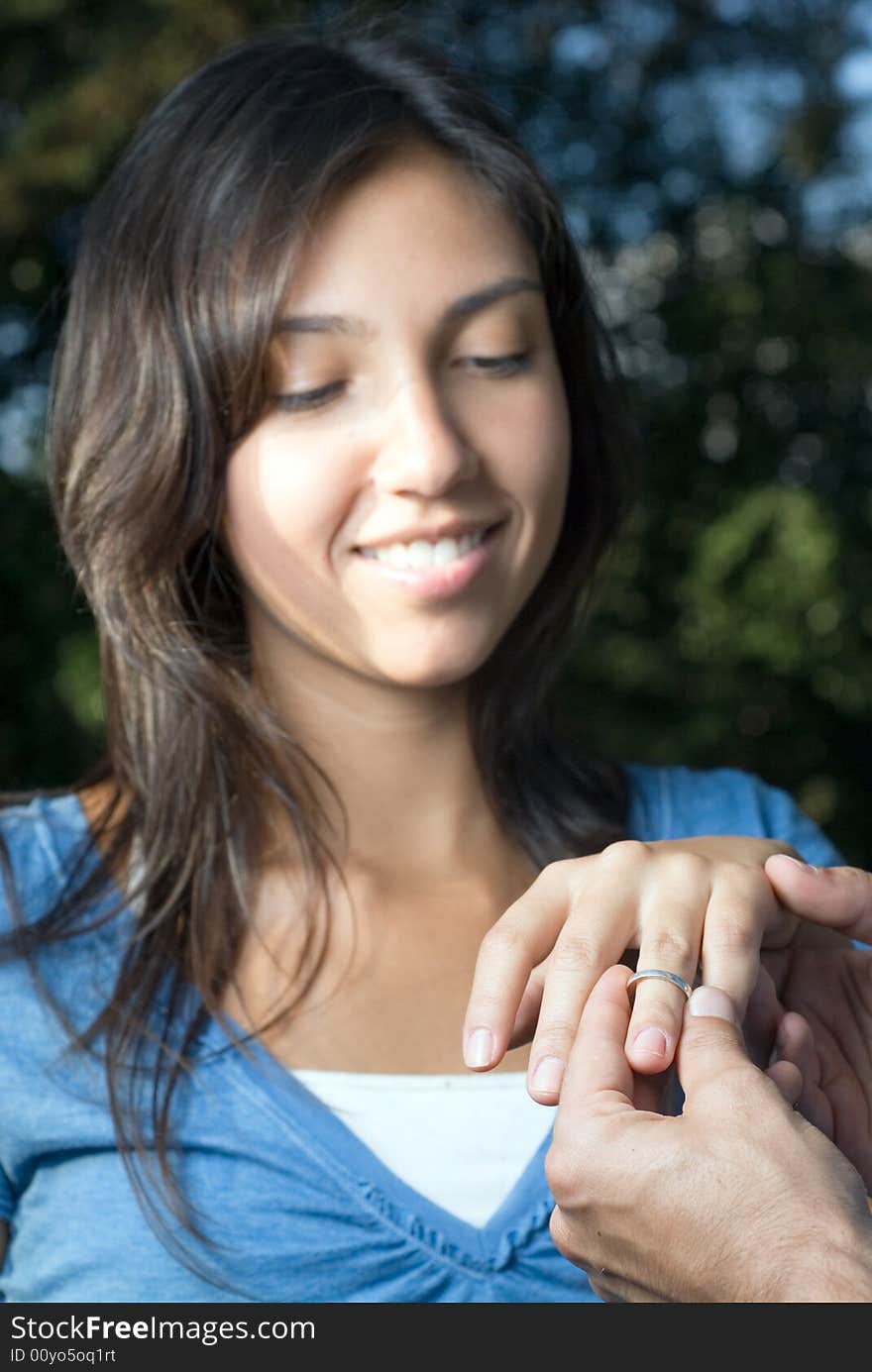 A woman smiles as someone slips an engagement ring upon her finger. Vertically framed photograph. A woman smiles as someone slips an engagement ring upon her finger. Vertically framed photograph.