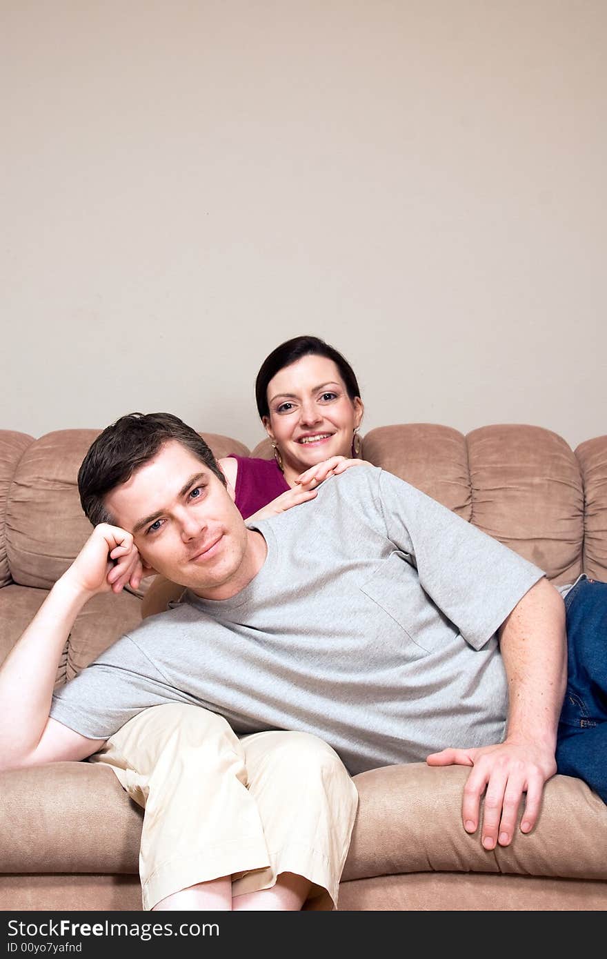 Smiling, happy couple sitting on a couch. He lays across her lap. Vertically framed photograph. Smiling, happy couple sitting on a couch. He lays across her lap. Vertically framed photograph