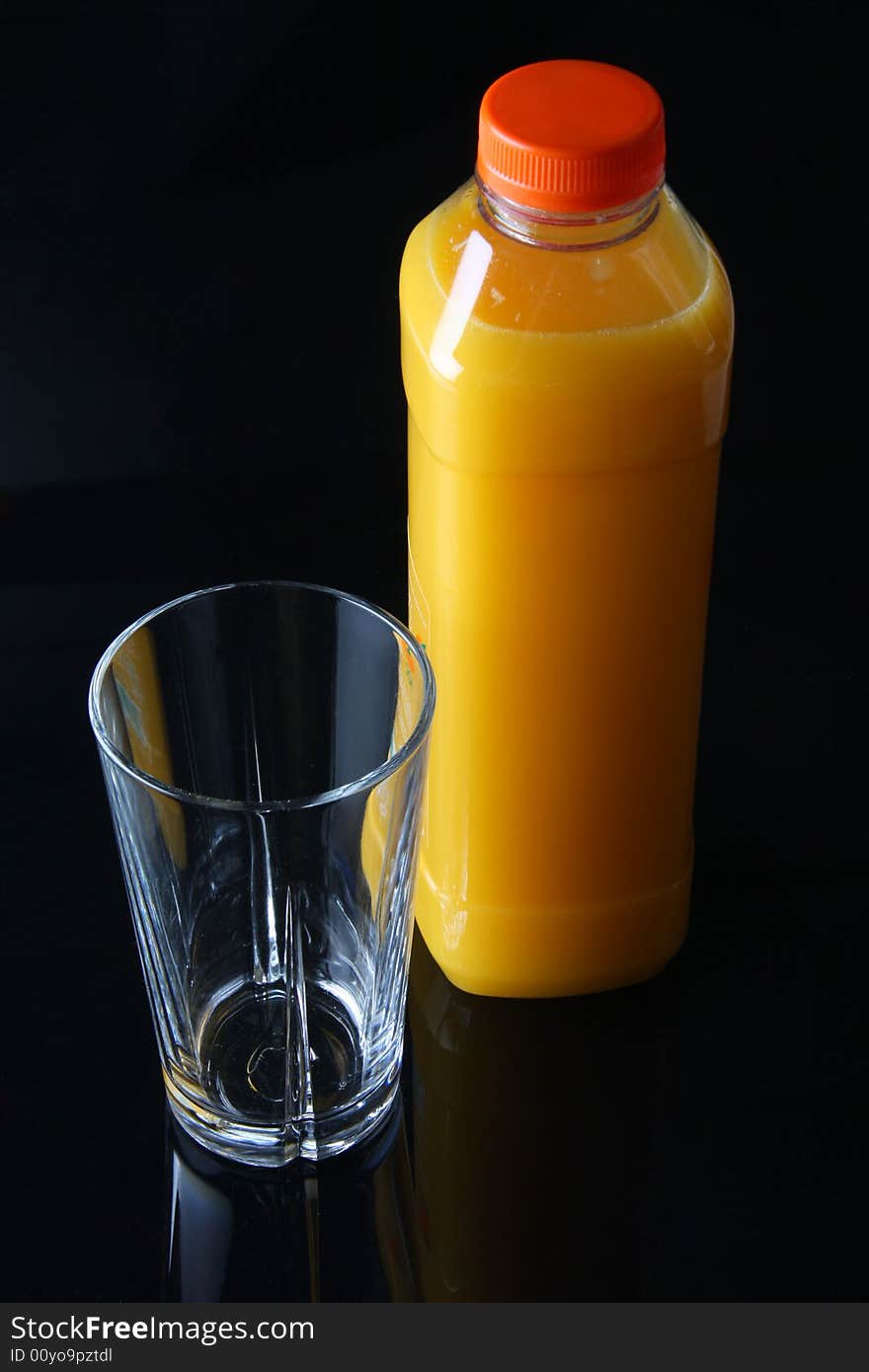 Fresh orange juice in a bottle, standing next to a empty glass, shot on black