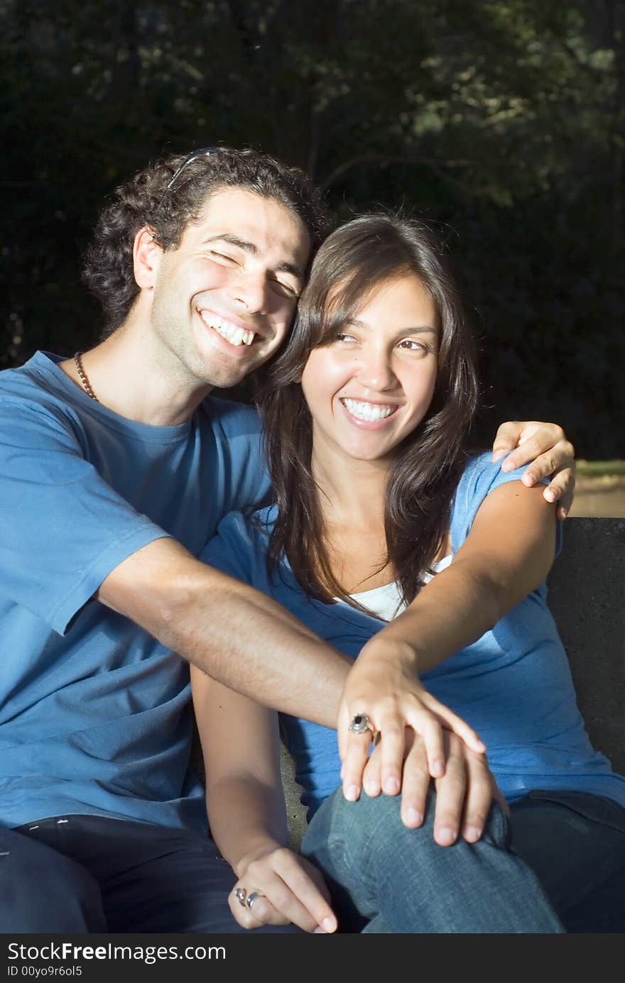 Happy, attractive couple sit in a park. They are smiling and embracing each other. Vertically framed photograph. Happy, attractive couple sit in a park. They are smiling and embracing each other. Vertically framed photograph