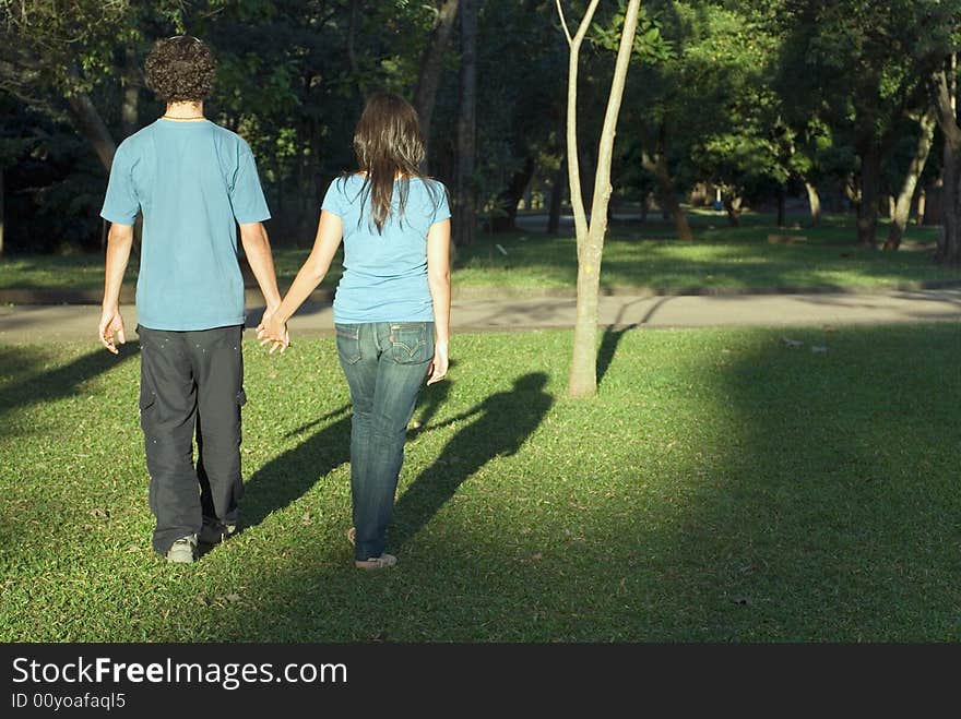 Couple holds hands as they walk through a park. Horizontally framed photograph. Couple holds hands as they walk through a park. Horizontally framed photograph.