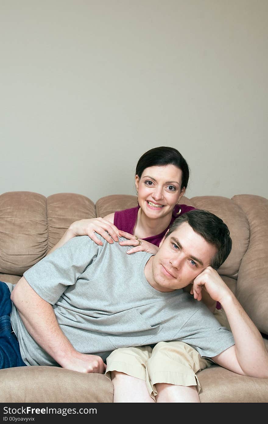 Smiling, happy couple sitting on a couch. He lays across her lap. Vertically framed photograph. Smiling, happy couple sitting on a couch. He lays across her lap. Vertically framed photograph