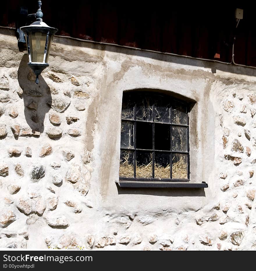 Old stony stable wall with a black window and a nice lamp. Old stony stable wall with a black window and a nice lamp