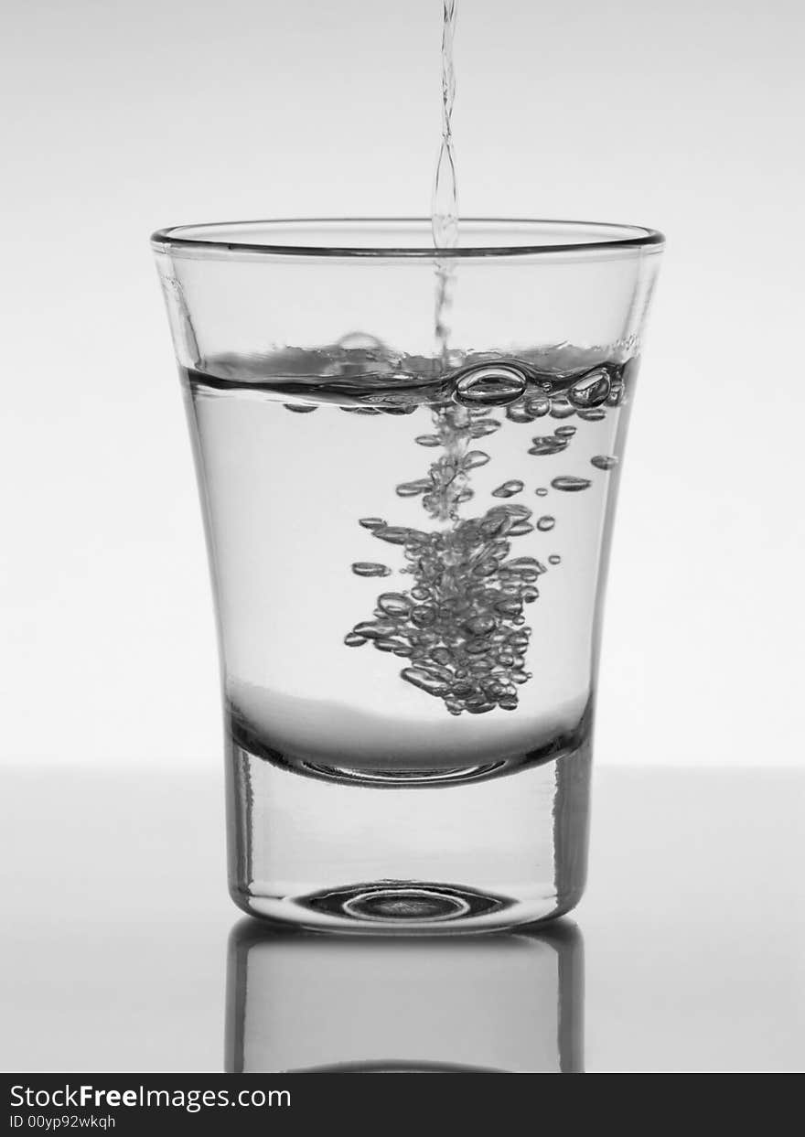 Water being poured into a glass with reflection on white background. Water being poured into a glass with reflection on white background.