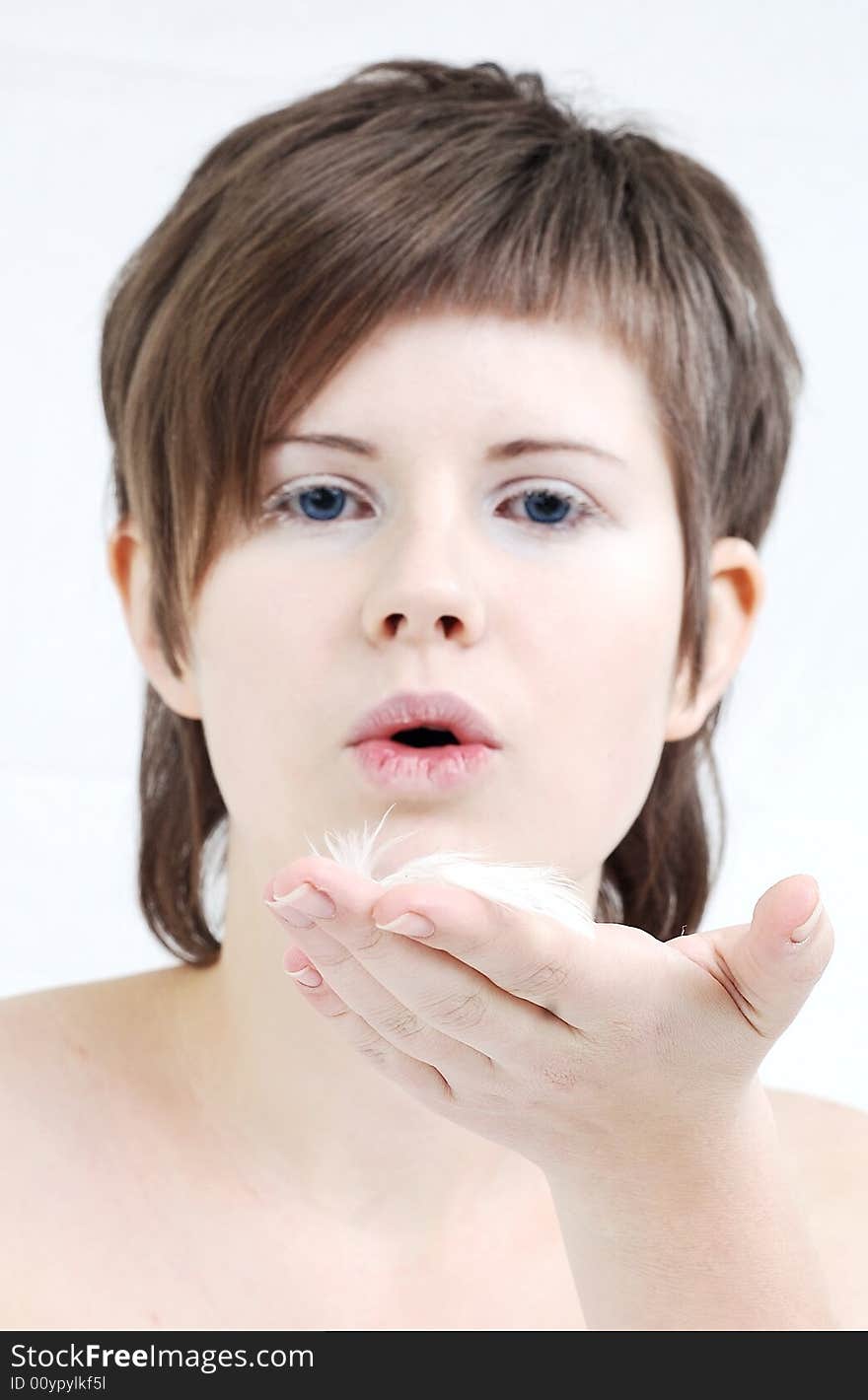 A cute girl blowing away a tiny feather from her hand