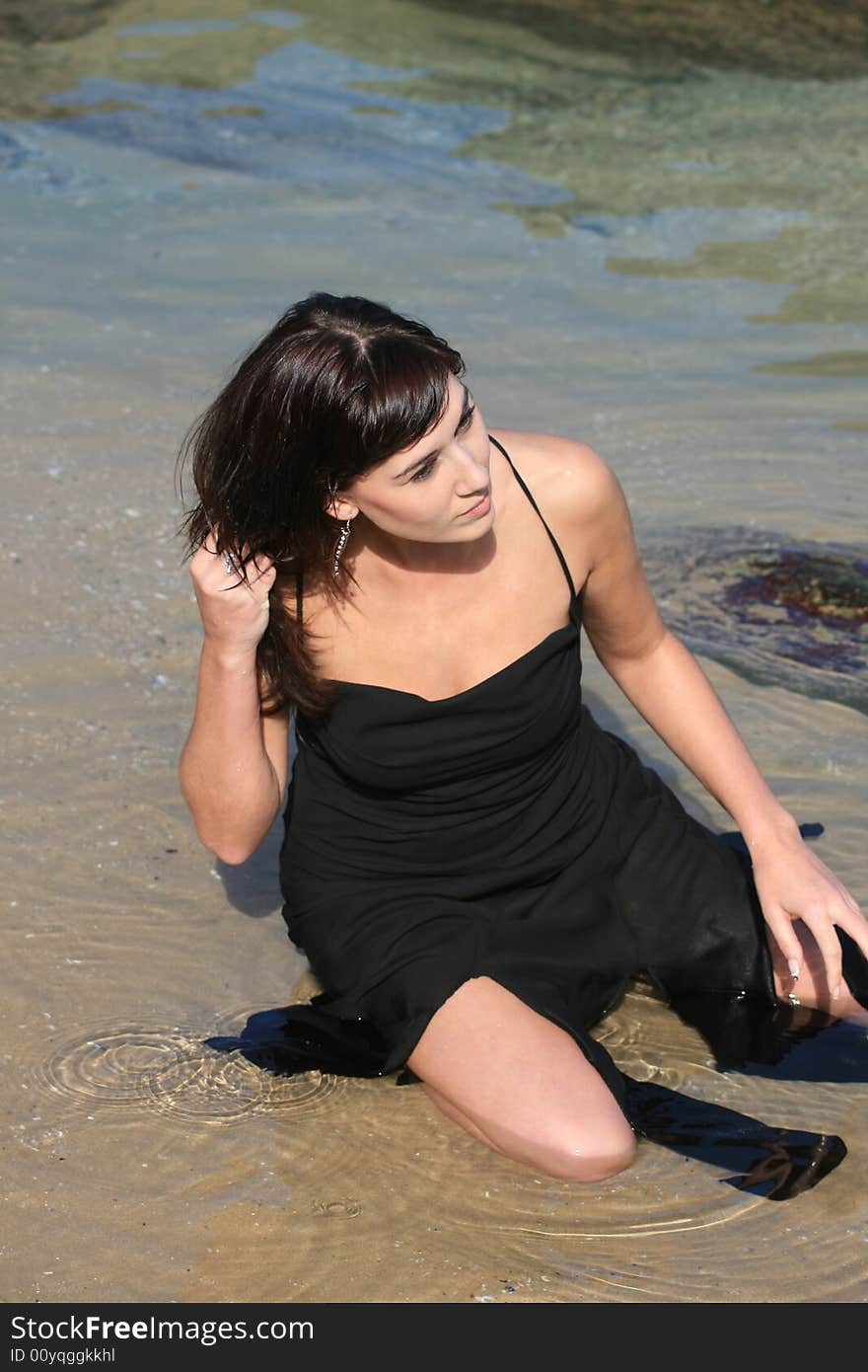 A beautiful white caucasian girl sitting in the water at the beach with her hand in her hair. A beautiful white caucasian girl sitting in the water at the beach with her hand in her hair