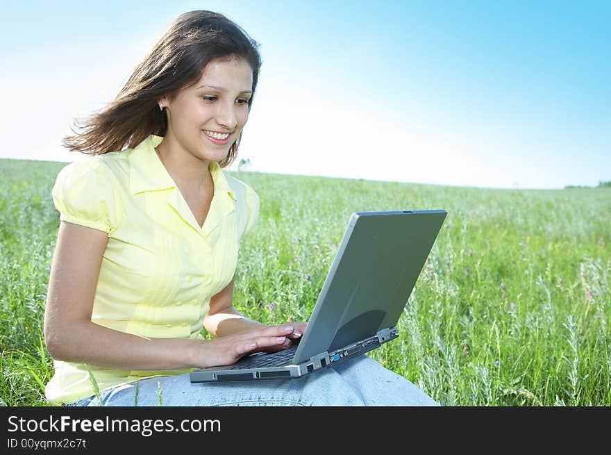 Pretty woman with laptop on the green grass under blue sky