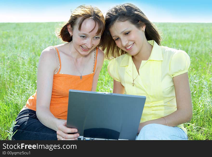 Two beautiful girls with laptop computer on green grass