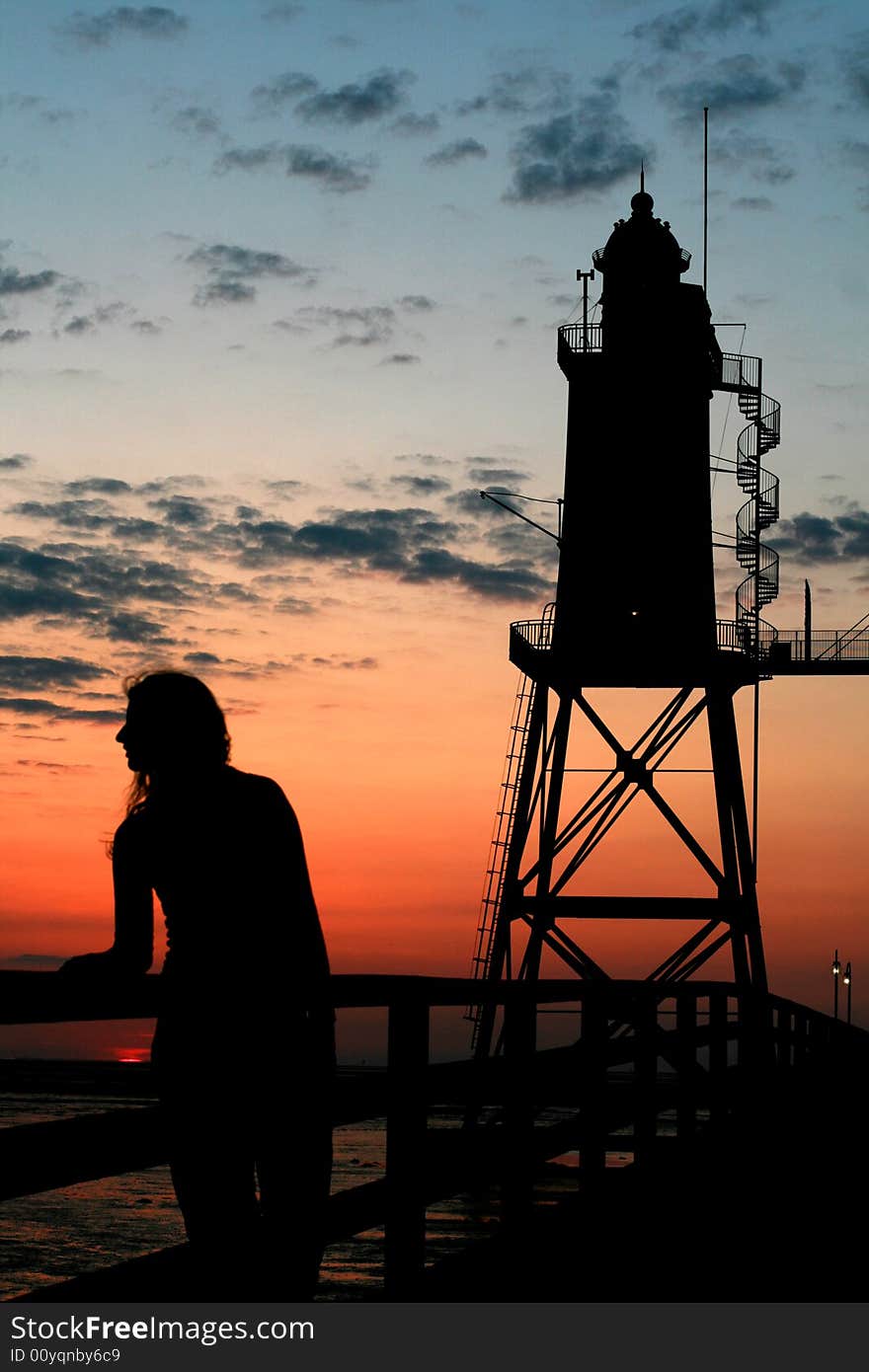 Silhouette of a girl in front of a lighthouse at sunset. Silhouette of a girl in front of a lighthouse at sunset