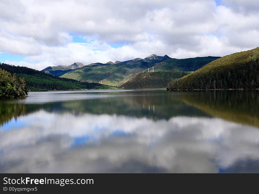 Lake in mountains surrounded by woods and the cloudy sky above it. Lake in mountains surrounded by woods and the cloudy sky above it.