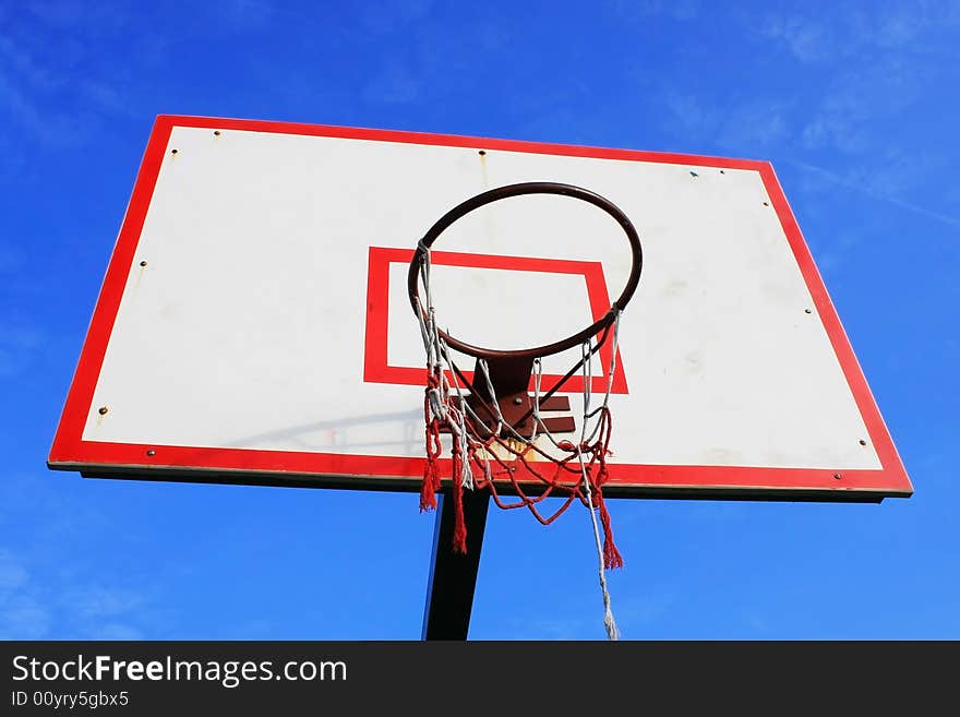 Basketball hoop with damaged net over blue sky.