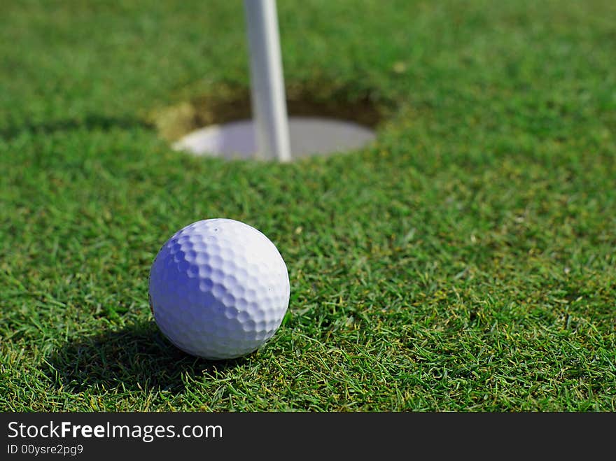 Golfball in front of the green grass hole. Golfball in front of the green grass hole