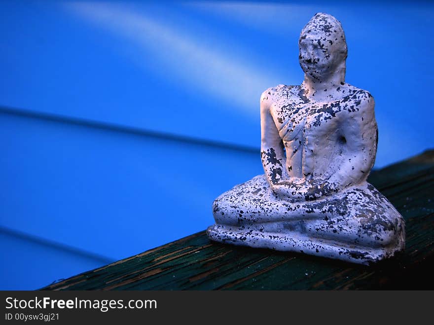 A Buddha on the rail of a deck, with a blue background, who appears to be receiving enlightenment. A Buddha on the rail of a deck, with a blue background, who appears to be receiving enlightenment.