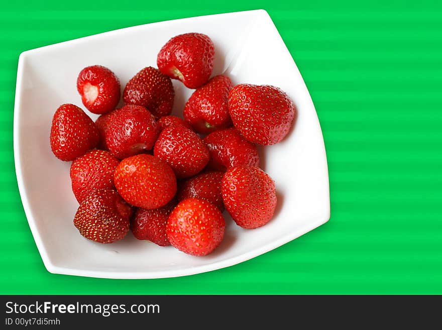 Fress summer strawberries in white bowl placed on striped green background. Fress summer strawberries in white bowl placed on striped green background