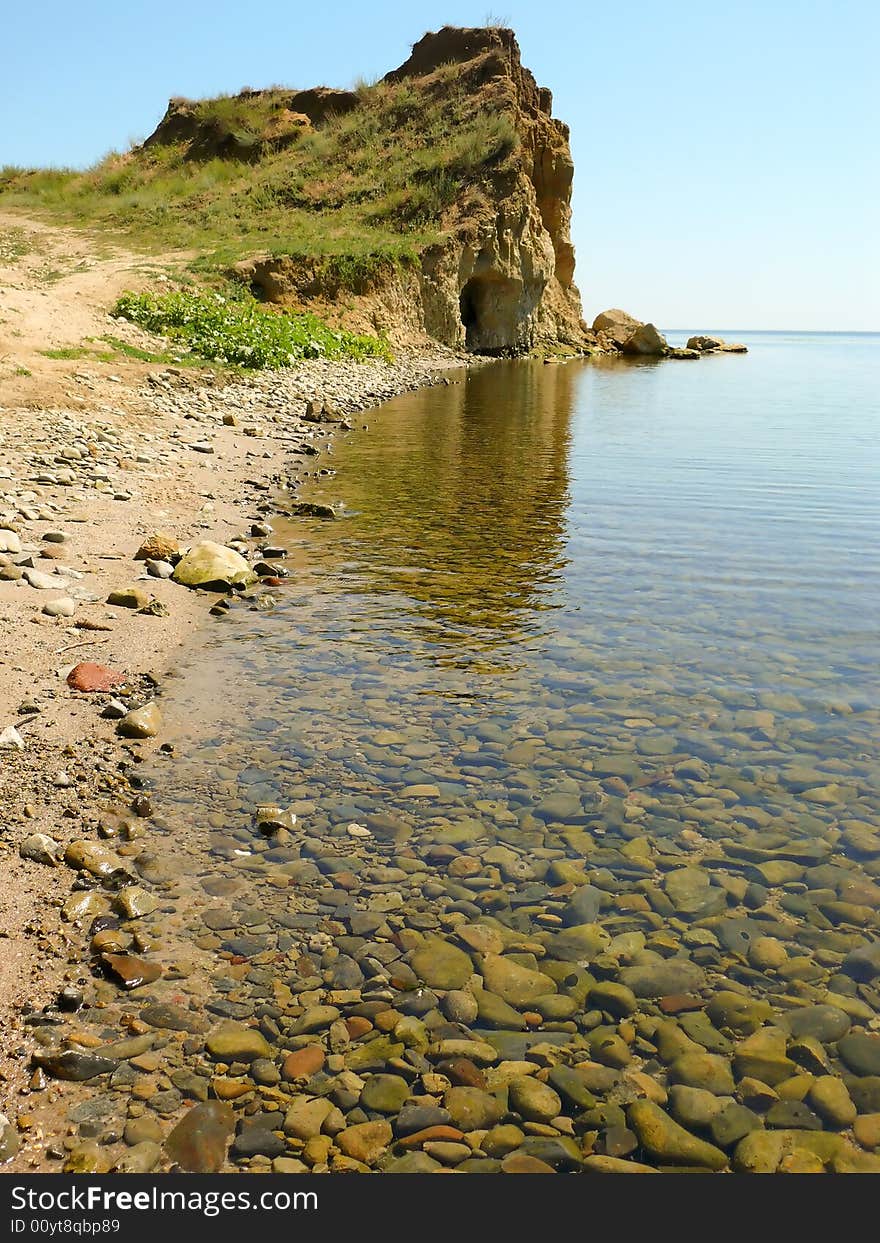 Beach. Quiet, transparent water, rocks on the bottom. The high cliff away.