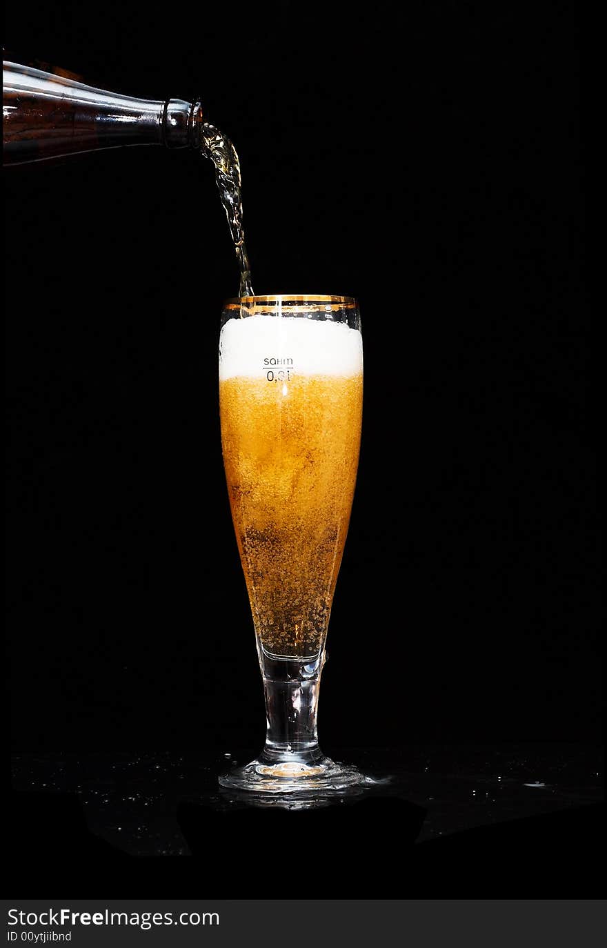 Cold gold beer pouring into a beer-glass on black.