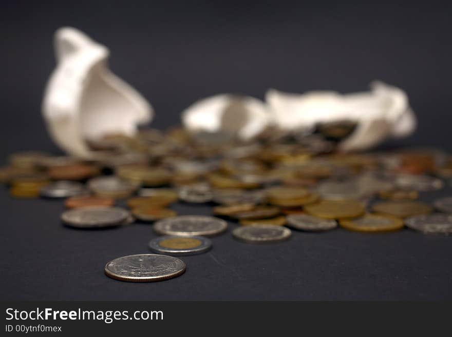 A broken piggy bank isolated on a dark background with loads of coins from around the world.