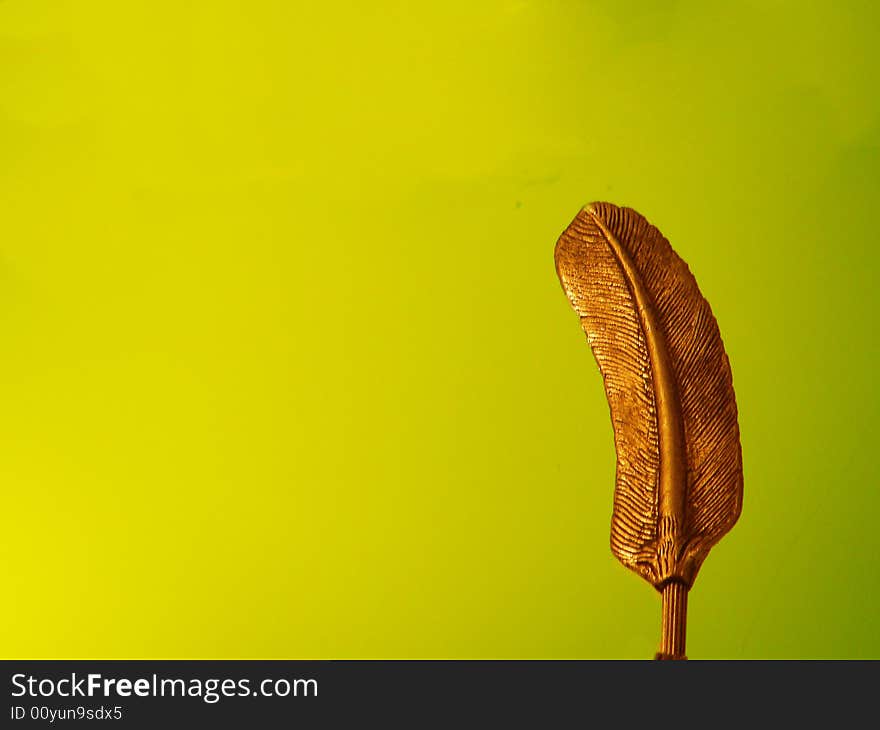 A bronze feather standing alone on a background of a brilliant apple green colored wall. A bronze feather standing alone on a background of a brilliant apple green colored wall