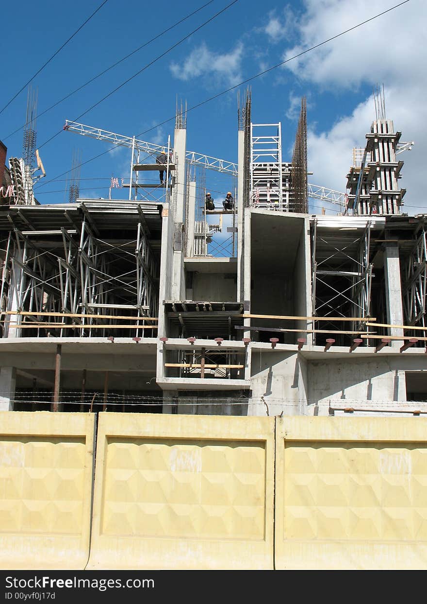 A building site, a hoisting crane and unfinished walls on the blue sky background.