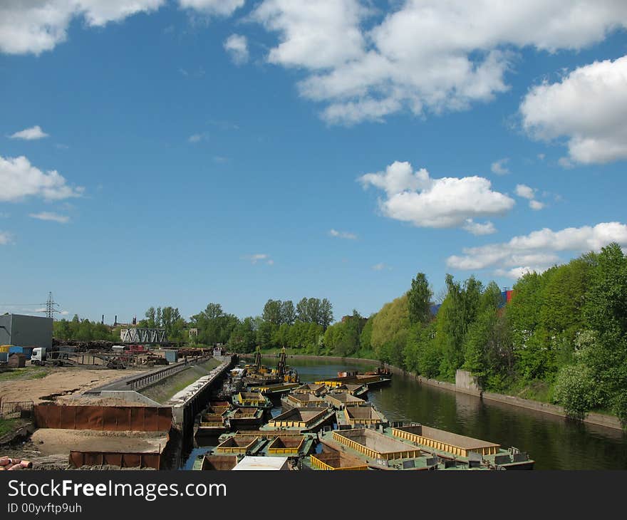 The barges on the canal. The industrial water landscape. The blue sky with overcast. Trees on the bank. Spring.