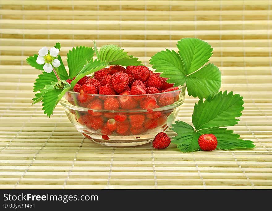 Red strawberry fruits with green leafs and flower in glass vase