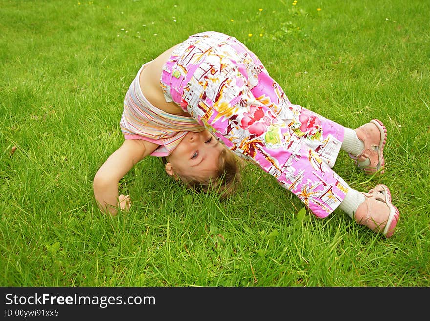 A little girl makes exercise on grass