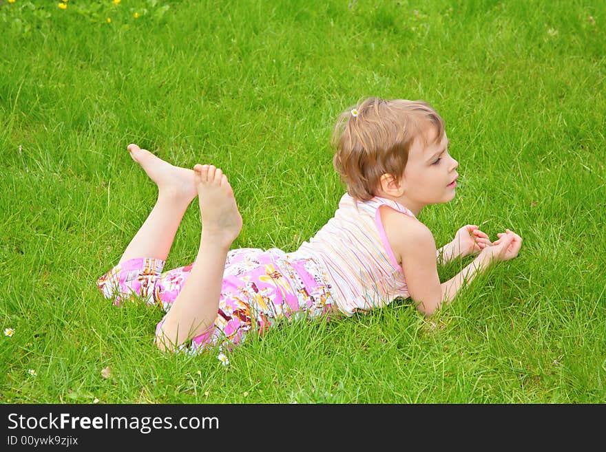 Little girl lies on grass on belly