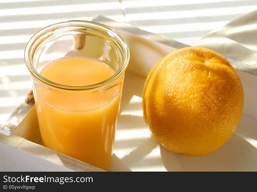 Orange juice and one orange on a tray