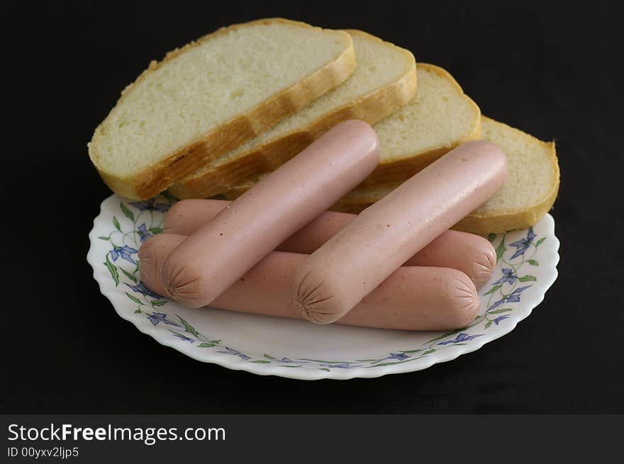 Several sausages with the slices of bread against the black background. Several sausages with the slices of bread against the black background