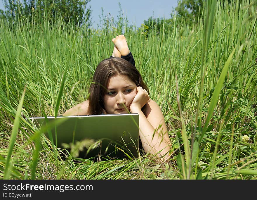 The girl works on a computer on a green grass. The girl works on a computer on a green grass