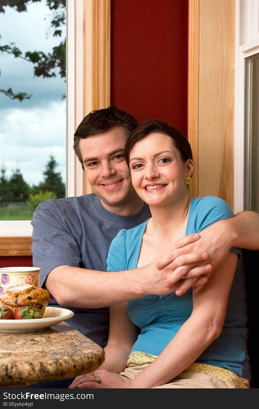 An attractive couple smiling over breakfast.  The man is hugging the woman.  Vertically framed shot. An attractive couple smiling over breakfast.  The man is hugging the woman.  Vertically framed shot.