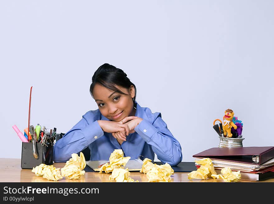 Teen girl smiling as she sits at a desk surrounded by crumpled paper, pens, pencils, and folders. Horizontally framed photograph. Teen girl smiling as she sits at a desk surrounded by crumpled paper, pens, pencils, and folders. Horizontally framed photograph