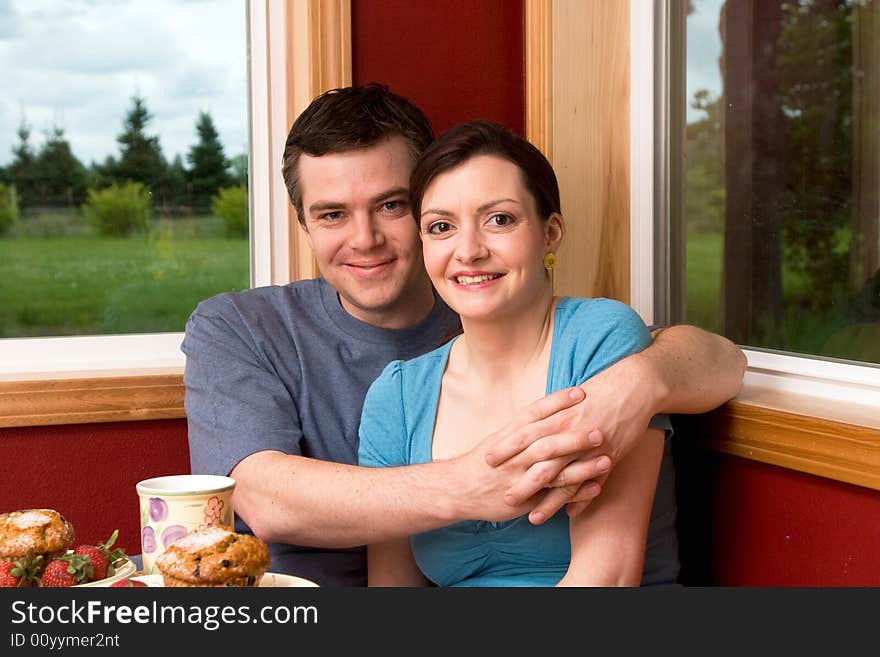 A couple smiling by large windows at home.  The man is hugging the woman.  Horizontally framed shot. A couple smiling by large windows at home.  The man is hugging the woman.  Horizontally framed shot.