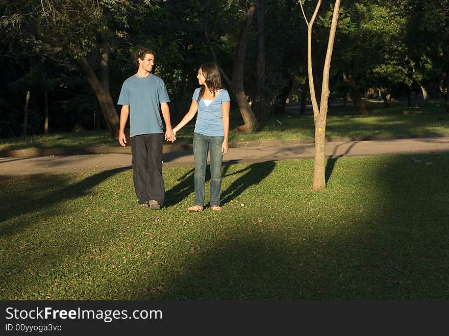 Couple holding hands walking in the park. Their shadows are seen behind them. Horizontally framed photograph. Couple holding hands walking in the park. Their shadows are seen behind them. Horizontally framed photograph