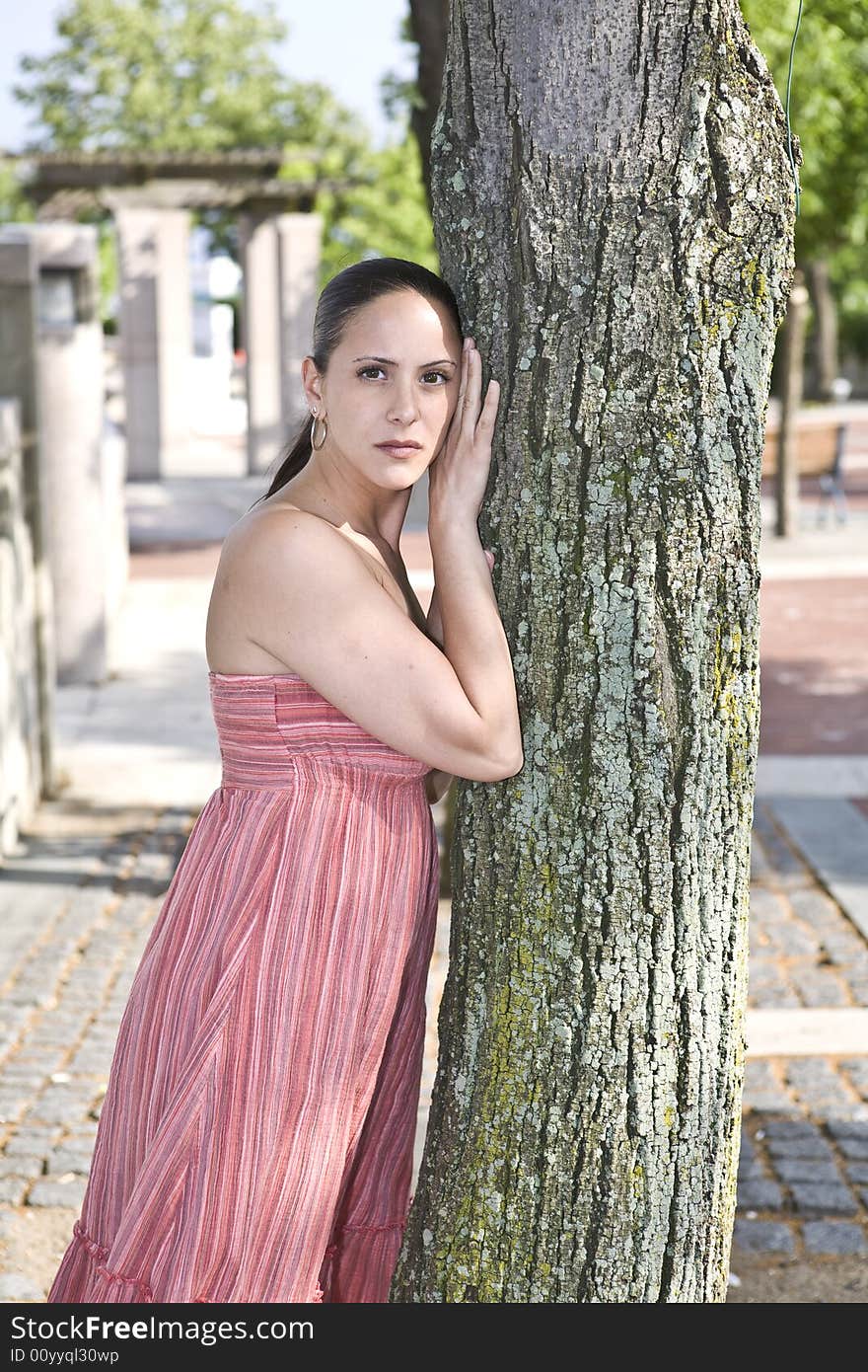 A beautiful young woman posing by a tree in a public park. A beautiful young woman posing by a tree in a public park