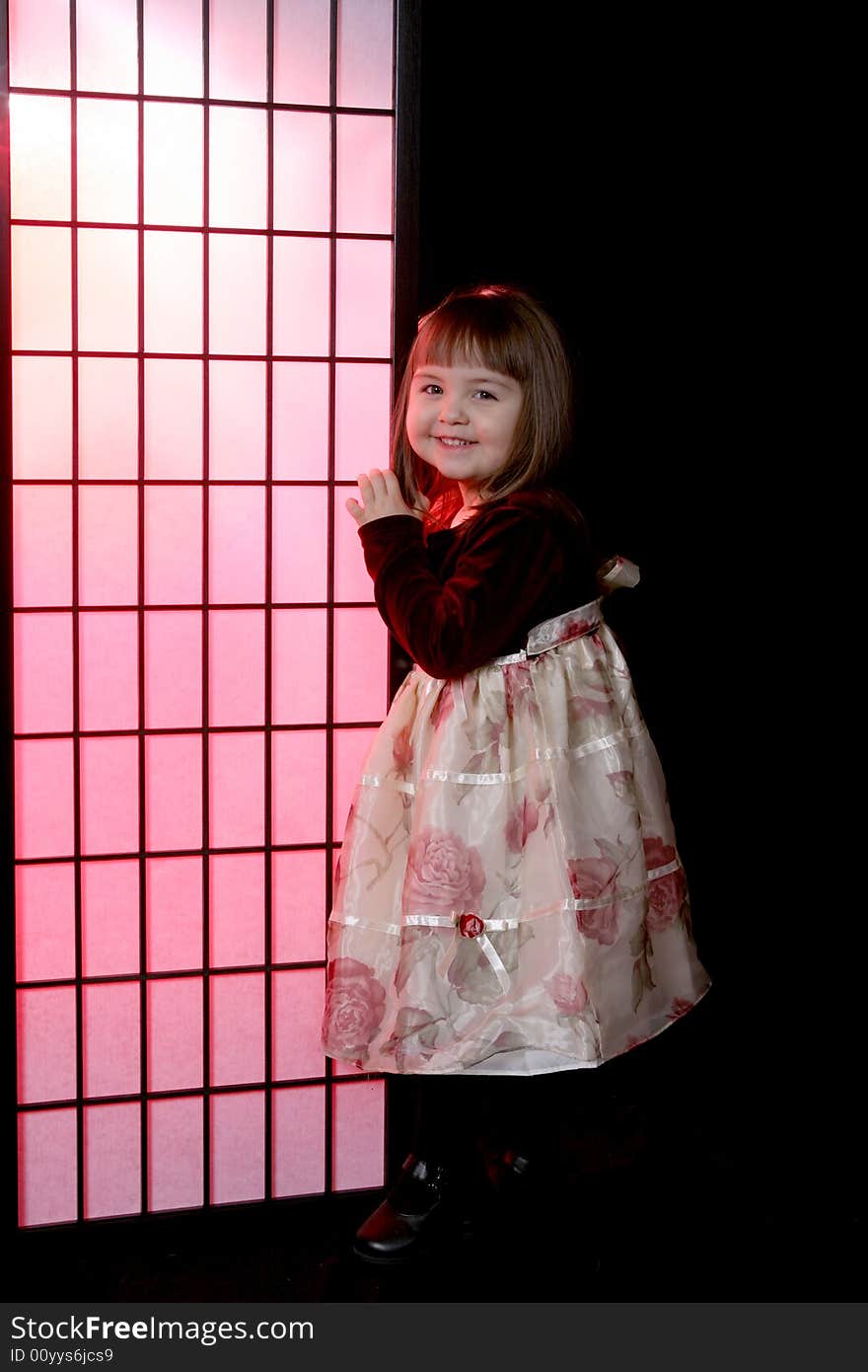 Pretty little girl in flowered party dress and standing next to a pink screen. Pretty little girl in flowered party dress and standing next to a pink screen.