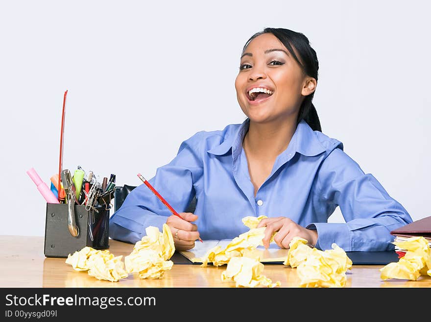 Teen girl laughs as she sits at a desk surrounded by crumpled paper, pens, pencils, and folders. Horizontally framed photograph. Teen girl laughs as she sits at a desk surrounded by crumpled paper, pens, pencils, and folders. Horizontally framed photograph