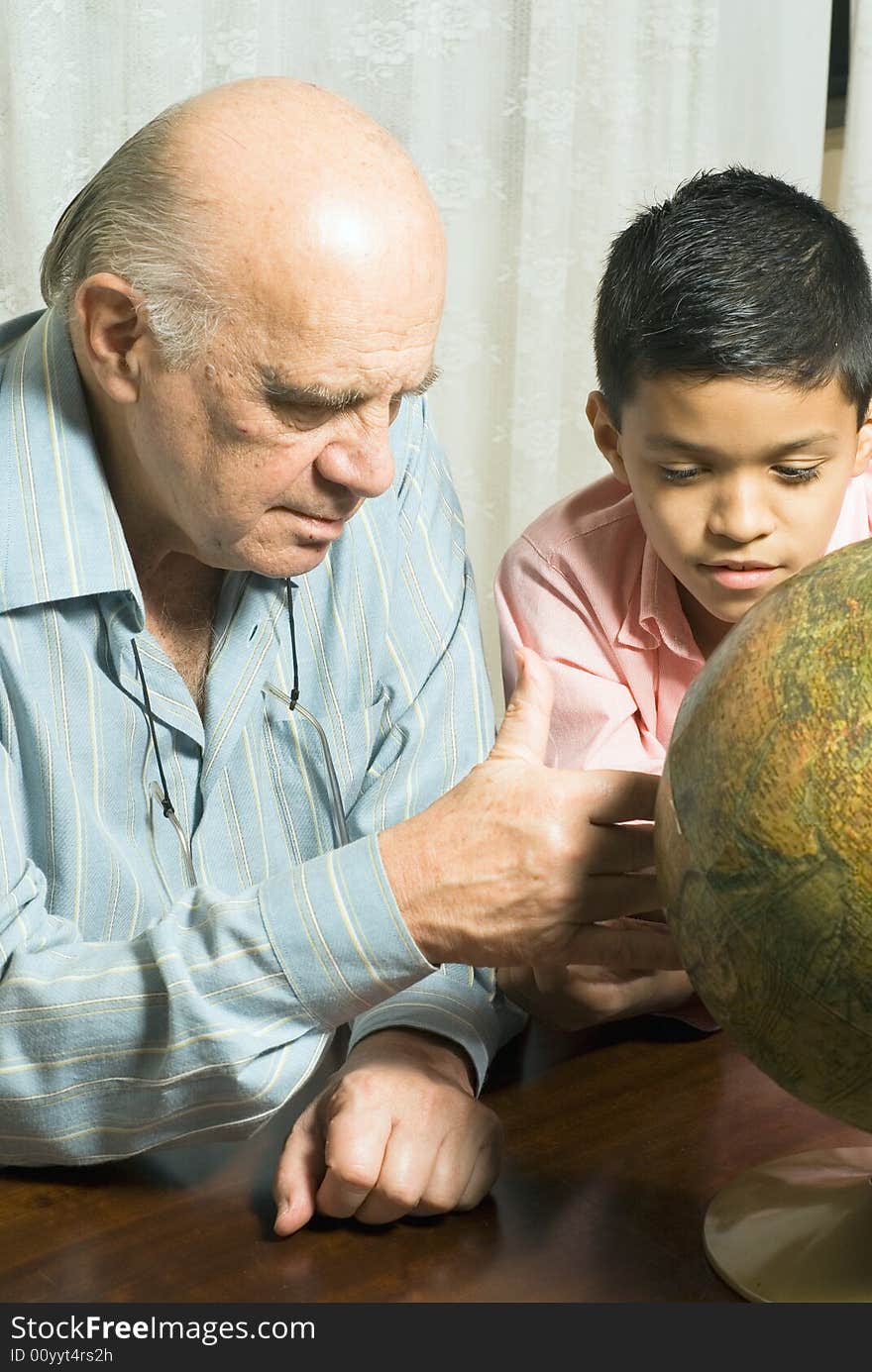 Grandfather and Grandson are seated at a table looking at a globe together. Vertically framed photograph. Grandfather and Grandson are seated at a table looking at a globe together. Vertically framed photograph.