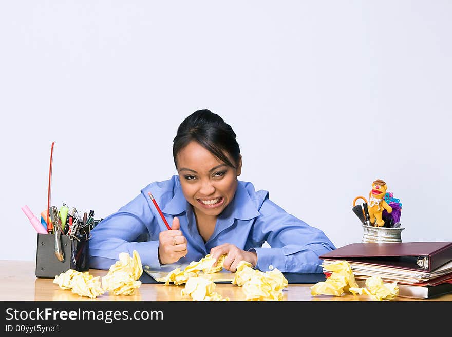 Teen girl looks stressed and angry as she sits at a desk surrounded by crumpled paper, pens, pencils, and folders. Horizontally framed photograph. Teen girl looks stressed and angry as she sits at a desk surrounded by crumpled paper, pens, pencils, and folders. Horizontally framed photograph