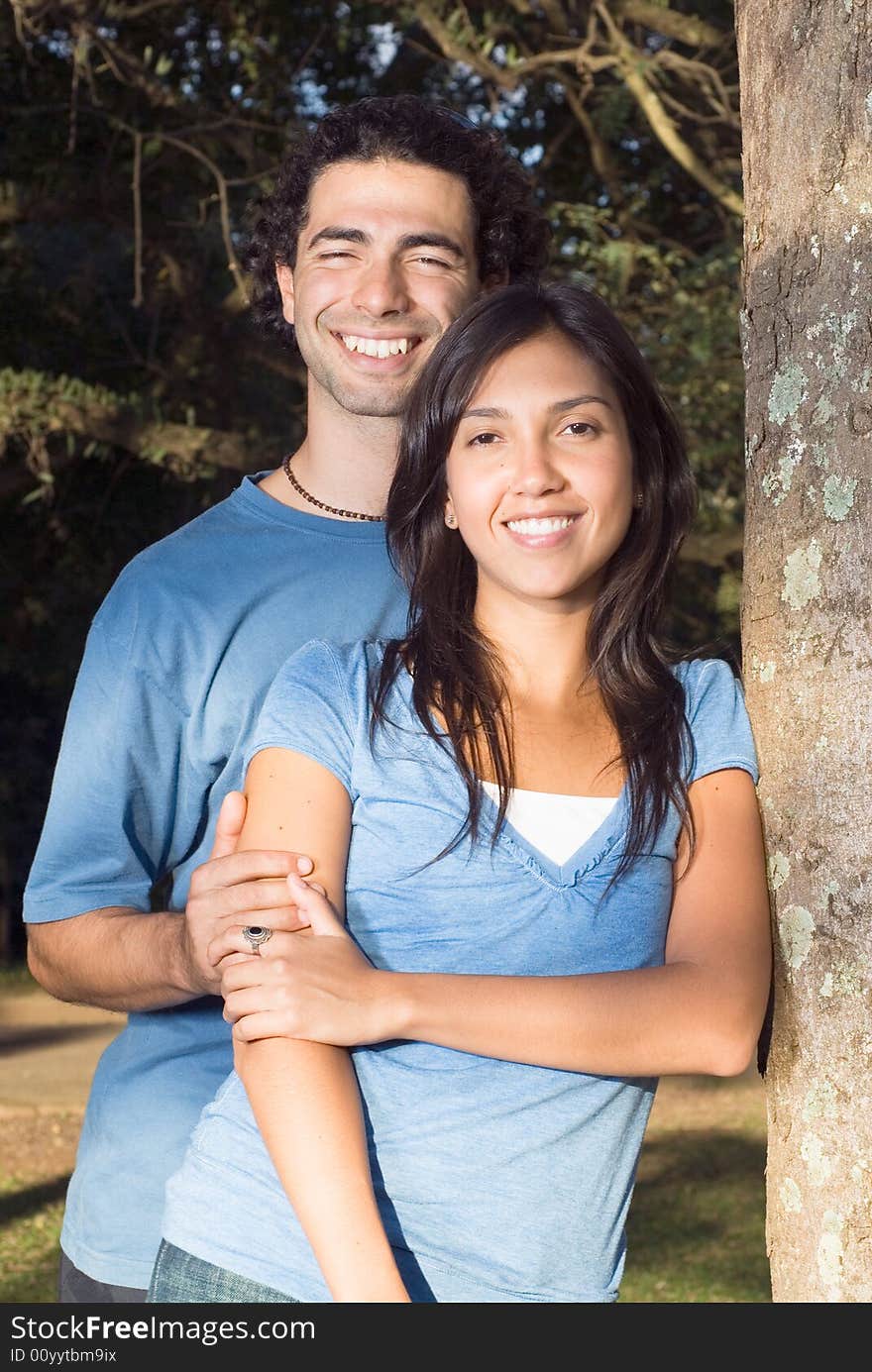 Happy couple hold each other and smile as they lean against a tree. Vertically framed photograph. Happy couple hold each other and smile as they lean against a tree. Vertically framed photograph