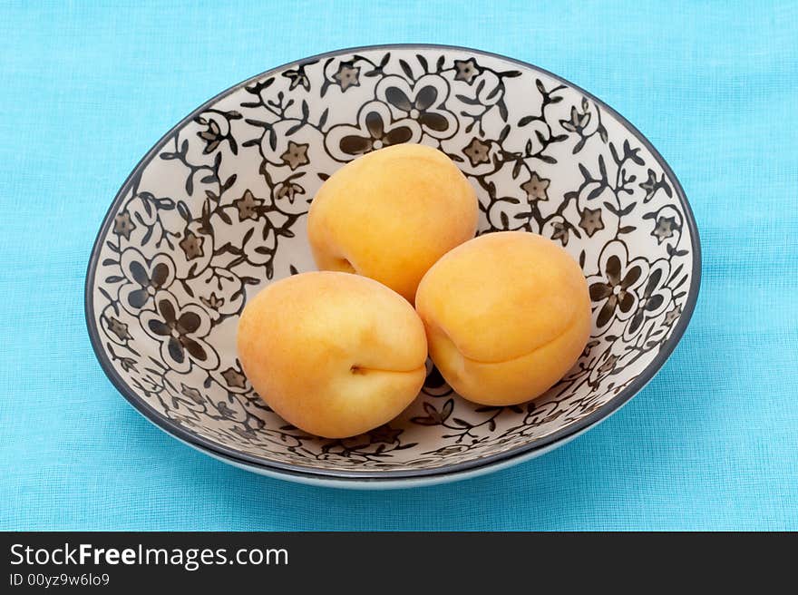 Three apricots in a bowl on blue fabric