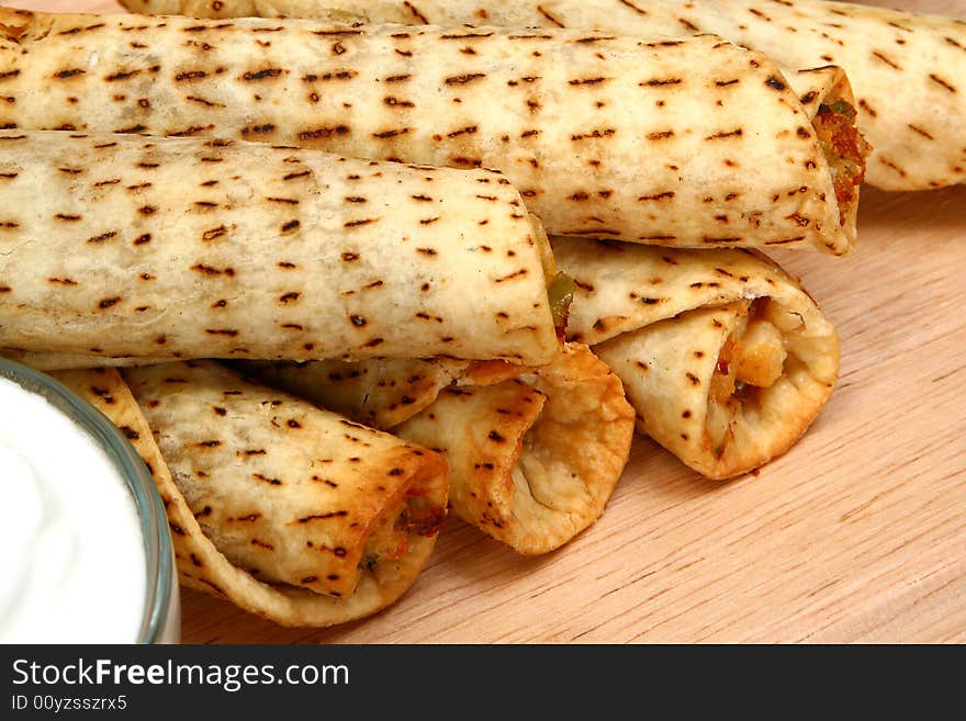 Stack of chicken taquitos with hot sauce and sour cream in kitchen or restaurant