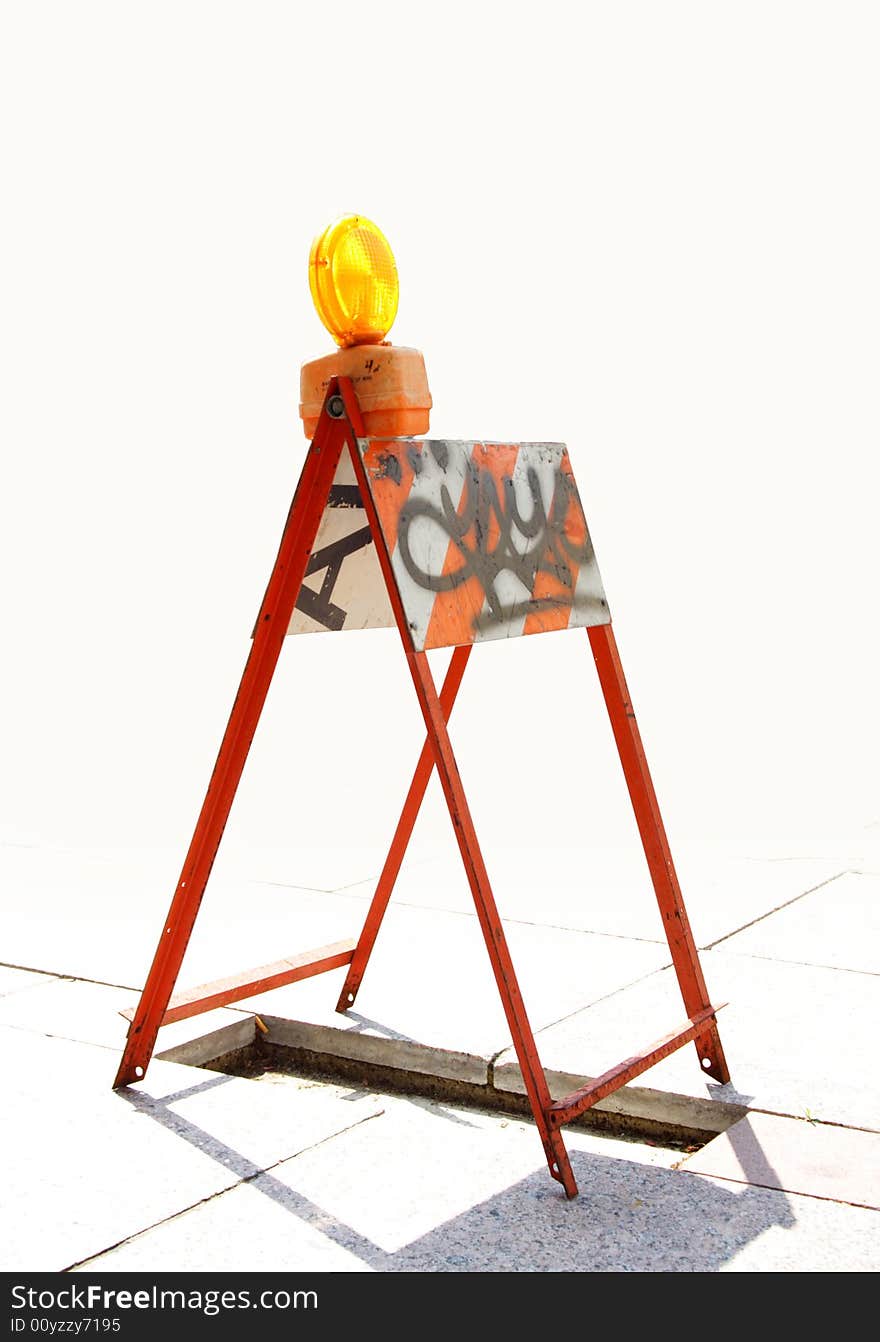 Orange reflector on a barricade covering an open pit on the sidewalk.