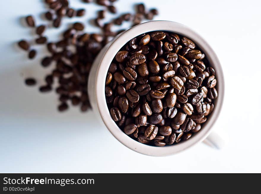 Whole bean coffee in mug isolated on white with beans scattered around mug