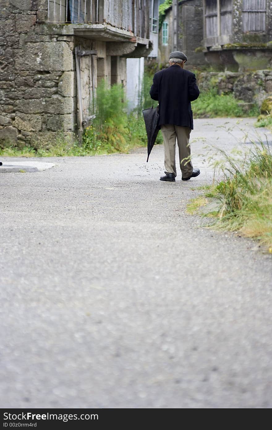 Old man with an umbrella strolling along a village path. Old man with an umbrella strolling along a village path