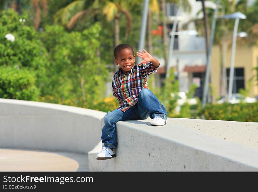 Young boy sitting on a concrete ledge and waiving. Young boy sitting on a concrete ledge and waiving.