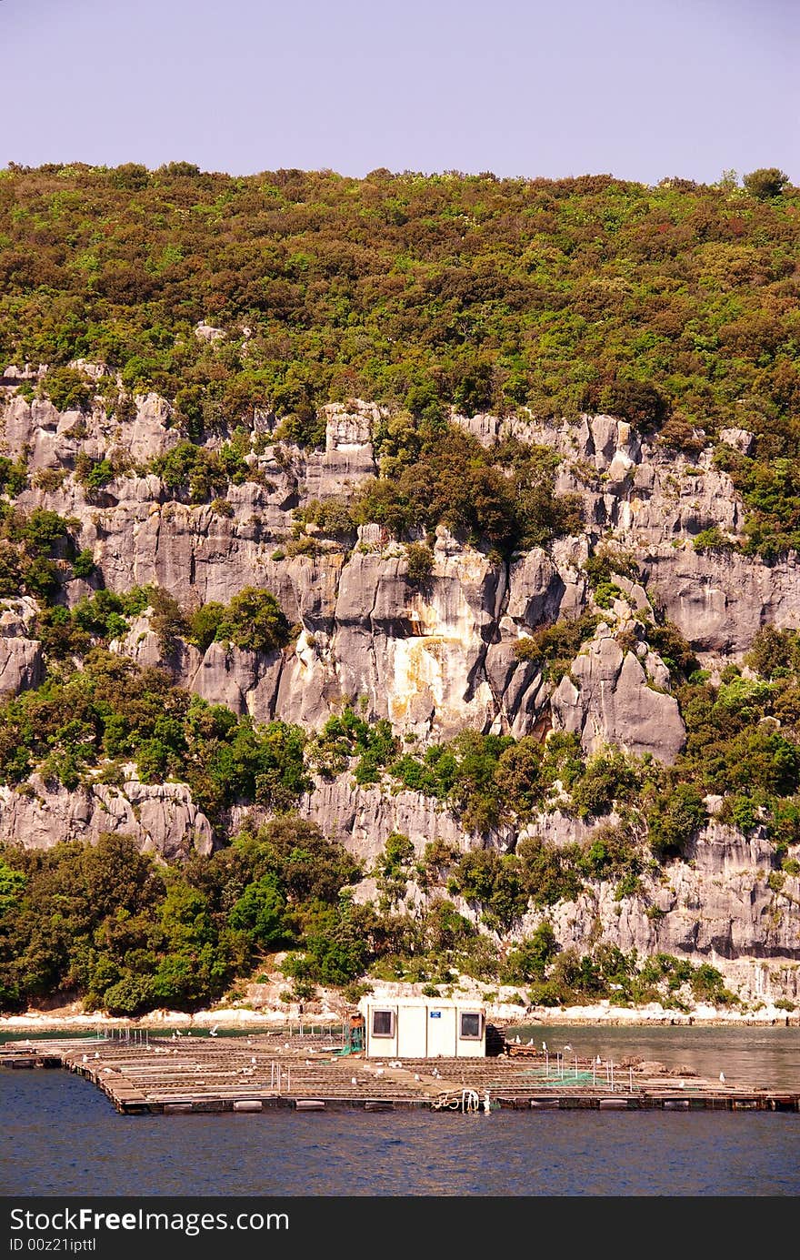 Rocks with in front a fish farm in the river