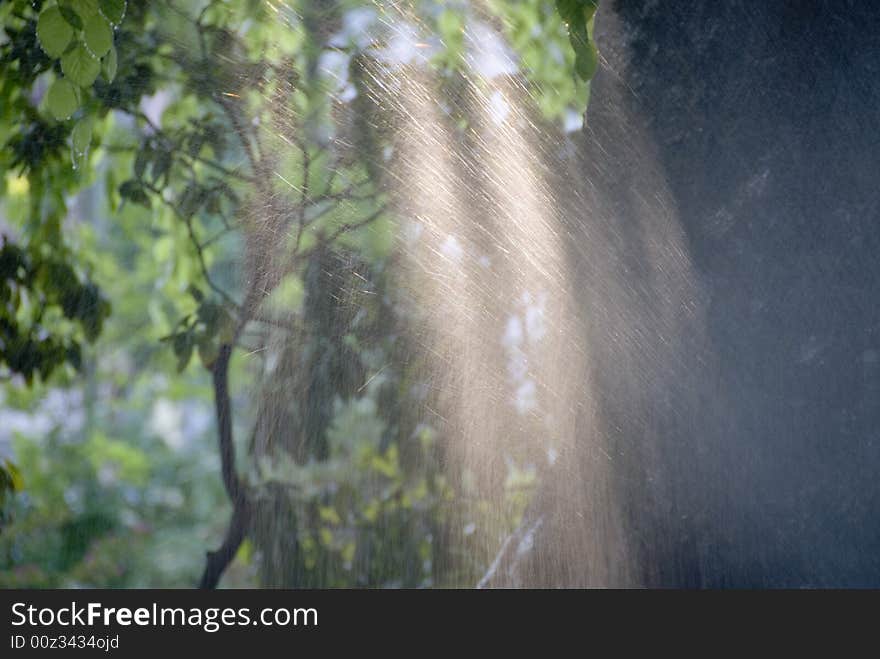 A park is watered by a sprinkler. A park is watered by a sprinkler