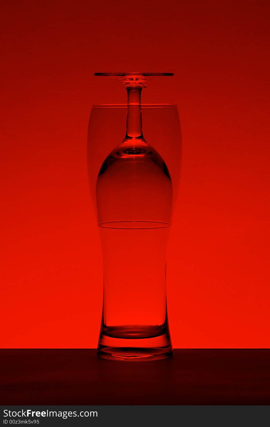 A wine and a beer glass put one into another to make optical effect. Red-toned for a dramatic look. A wine and a beer glass put one into another to make optical effect. Red-toned for a dramatic look.