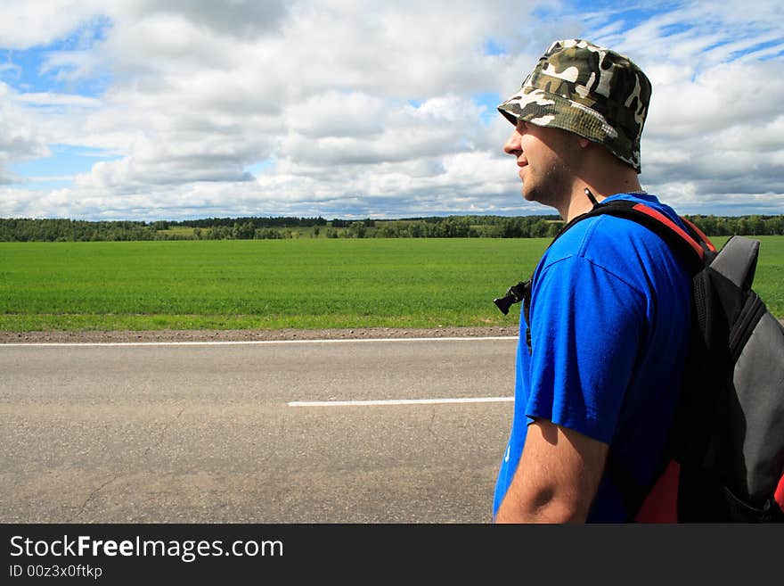 Man on a roadside of road on a background of clouds and the blue sky. Man on a roadside of road on a background of clouds and the blue sky